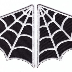 May include: Two black spiderweb patches with white stitching. Each patch is shaped like a stylized wing or fan, with a web design. The patches are likely for decorative purposes, such as sewing onto clothing or accessories.