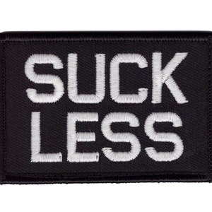May include: Black rectangular patch with white embroidered text that reads "SUCK LESS". The patch has a woven texture and a stitched border. The text is in a bold, sans-serif font.