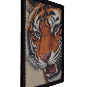 Op de afbeelding: Een rechthoekige patch met een gedetailleerde illustratie van een tijgergezicht. De tijger heeft oranje en zwarte strepen, met een roze neus en een open mond die tanden laat zien. De patch is omlijst door een zwarte rand.
