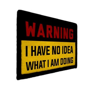 May include: A rectangular patch with the word "WARNING" in red letters above a yellow rectangle. The yellow rectangle contains the text "I HAVE NO IDEA WHAT I AM DOING" in black letters. The patch has a black border.