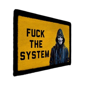 May include: A rectangular patch with a yellow background and black border. The text "FUCK THE SYSTEM" is in bold black letters. A graphic of a person wearing a Guy Fawkes mask and a hooded jacket is on the right.