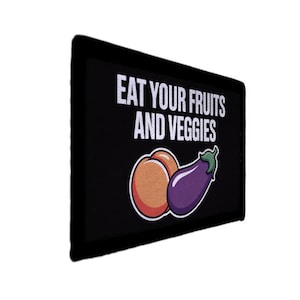May include: Black rectangular sign with the text "EAT YOUR FRUITS AND VEGGIES" in white. Below the text are illustrations of a peach and an eggplant. The peach is orange and the eggplant is purple.