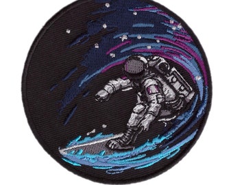 May include: Embroidered patch featuring an astronaut surfing a cosmic wave. The patch is circular, with a black background. The astronaut is in a spacesuit, riding a wave of blue, purple, and white. Stars are visible in the background.