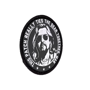 Pode incluir: Um patch preto e branco com o texto "THIS PATCH REALLY TIES THE GEAR TOGETHER, MAN." O patch apresenta um retrato estilizado de um homem usando óculos de sol.