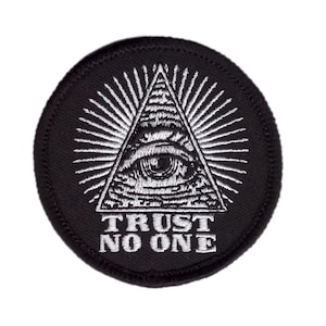 Könnte beinhalten: Ein runder, schwarzer Aufnäher mit einem weißen Design. Es zeigt ein weißes Auge in einem Dreieck, umgeben von Strahlenlinien. Der Text "TRUST NO ONE" ist darunter in Weiß gedruckt.