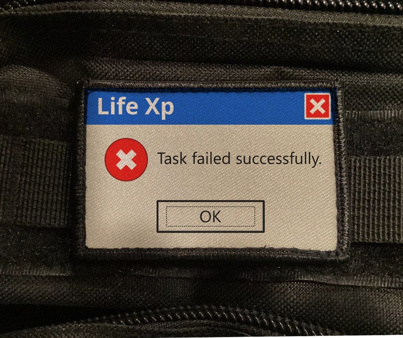 May include: A rectangular patch with a blue top section that reads "Life Xp" and a red "X" in the upper right corner. The text "Task failed successfully." is below the "Life Xp" text. The patch has an "OK" button.