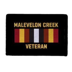 May include: Black rectangular patch with gold lettering: "MALEVELON CREEK VETERAN." A horizontal stripe features red, gold, brown, black, white, brown, gold, and red. The patch is rectangular.
