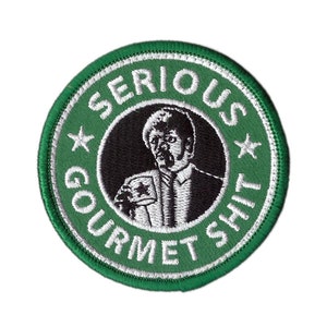May include: Circular embroidered patch with a green border and the words "SERIOUS GOURMET SHIT" in white. The patch features a black and white image of a man in a suit. Two white stars are on the patch.