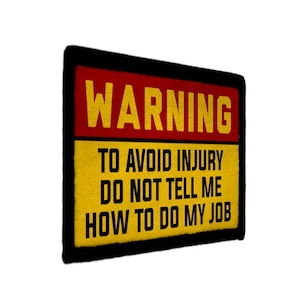 May include: Embroidered patch with the word "WARNING" in yellow on a red background. Below, the text reads "TO AVOID INJURY DO NOT TELL ME HOW TO DO MY JOB" in yellow on a yellow background, framed by a black border.
