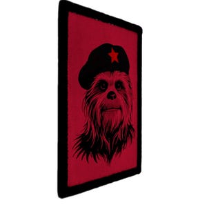 May include: A rectangular patch with a red background and a black border. The patch features a black illustration of a furry creature wearing a black beret with a red star. The creature has a long beard.