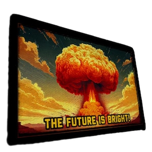May include: A framed art print depicting a nuclear explosion in a stylized manner. The image shows a large, orange and red mushroom cloud set against a backdrop of yellow and blue skies. The text "THE FUTURE IS BRIGHT!" is displayed in a bold, yellow font.