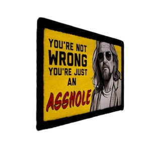 Op de afbeelding: Rechthoekige patch met een gele achtergrond en zwarte rand. De tekst "YOU'RE NOT WRONG YOU'RE JUST AN ASSHOLE" staat in zwart en rood. Een zwart-wit illustratie van een man met een zonnebril staat rechts.