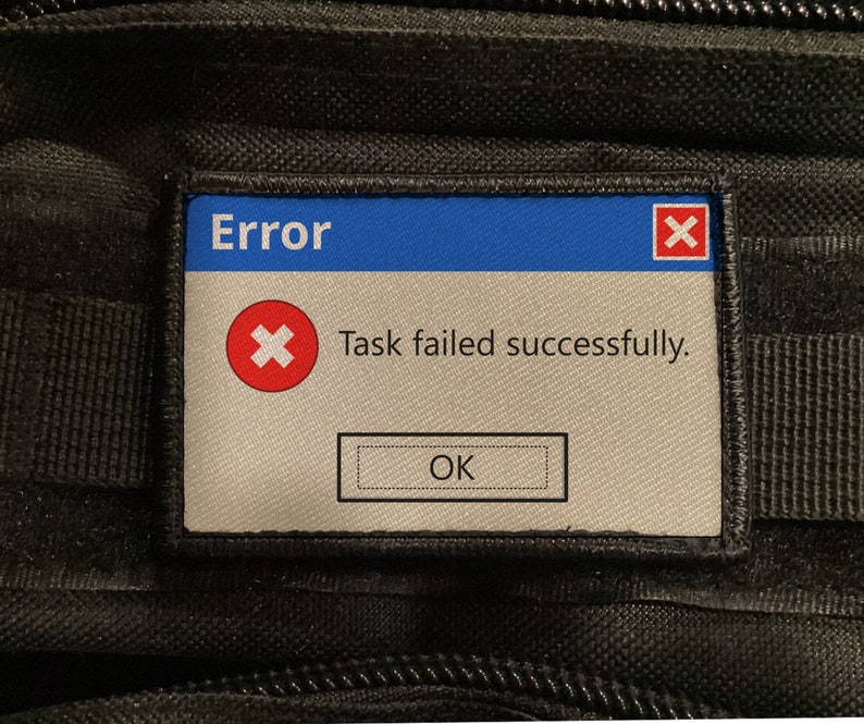 May include: A rectangular patch with a blue top section labelled "Error." Below, a red "X" icon is above the text "Task failed successfully." An "OK" button is at the bottom. The patch is set against a black, textured background.