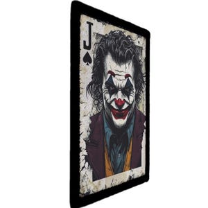 Pode incluir: Uma carta de jogar, o Valete de Espadas, com uma ilustração detalhada do personagem Joker. O Joker tem pintura facial branca, lábios vermelhos e maquilhagem verde e vermelha para os olhos. A carta tem uma borda preta e um aspeto vintage desgastado.
