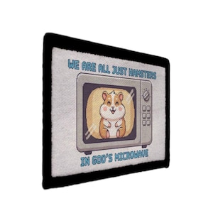 May include: A rectangular patch with a black border featuring a cartoon microwave. Inside the microwave is a smiling hamster. The text above reads "WE ARE ALL JUST HAMSTERS" and below "IN GOD'S MICROWAVE."