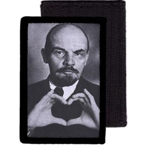 Könnte beinhalten: Schwarz-weißer Aufnäher mit einem Porträt eines Mannes, der mit seinen Händen ein Herz formt. Der Aufnäher hat einen schwarzen Rand und eine Klettverschlussrückseite.