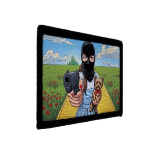 May include: A rectangular wall art print featuring a comic-style illustration of a figure in a black balaclava holding a handgun, wearing a blue gingham dress, and carrying a small brown dog with a red bow, set on a yellow brick road.