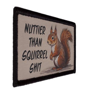 May include: A rectangular patch with a black border and the text "NUTTIER THAN SQUIRREL SHIT". The patch features a detailed illustration of a brown squirrel with a fluffy tail.