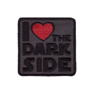 以下が含まれることがあります： 黒い正方形のパッチで、「I ❤️ THE DARK SIDE」というフレーズが黒い糸で刺繍されています。ハートは赤色です。このパッチは、衣服やアクセサリーに縫い付けるように設計されています。
