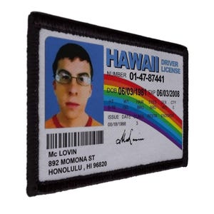 May include: A rectangular patch featuring a photo ID with the text "HAWAII DRIVER LICENSE." The ID includes a photo of a person wearing glasses, a rainbow design, and the name "Mc LOVIN." The patch has a black border.