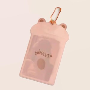 May include: A light pink, translucent cardholder shaped like a bear with small ear details at the top. The cardholder has a small orange lanyard attached. The word "Hisocute" is printed in cursive on the front.