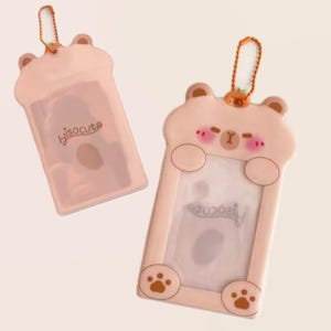 May include: Two pink bear-shaped card holders with a clear window. One has the text "hisocute". The bear design includes paw prints, a small nose, and blush marks. Each holder has a gold-coloured chain.