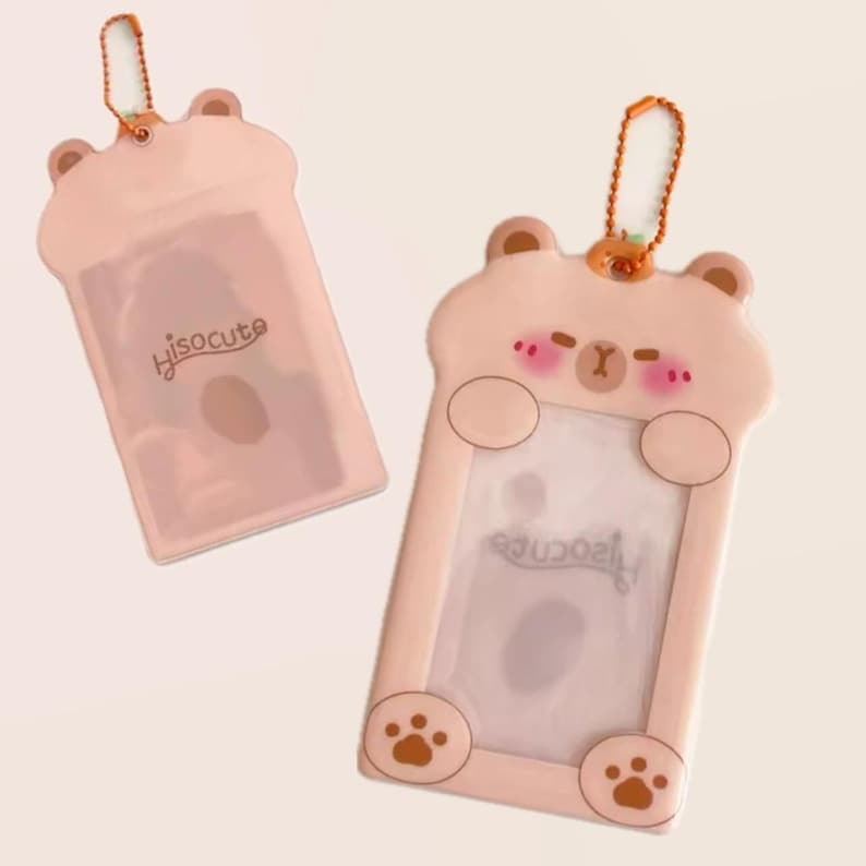 May include: Two pink bear-shaped card holders with a clear window. One has the text "hisocute". The bear design includes paw prints, a small nose, and blush marks. Each holder has a gold-coloured chain.