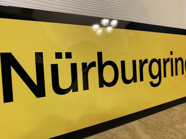 May include: A yellow sign with black lettering that reads "N&uuml;rburgring".