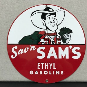 Puede incluir: Un letrero redondo de metal rojo y blanco con un vaquero de dibujos animados sosteniendo dinero. El letrero dice "Saw'n SAM'S ETHYL GASOLINE".