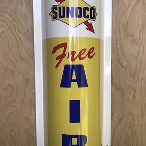 May include: A yellow and white cylindrical sign with a red arrow and the text "SUNOCO" in a white diamond. The sign also has the text "Free Air" in red and blue letters.