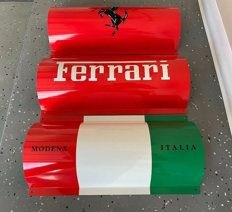 May include: Three red, white, and green metal signs with curved edges. The top sign features a black prancing horse logo and the word "Ferrari". The middle sign says "Ferrari" in white letters. The bottom sign has the words "MODENA" and "ITALIA" in black letters.