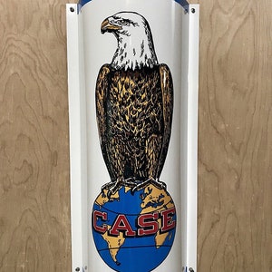 May include: A vintage metal sign with a blue and white border. The sign features a bald eagle standing on a globe with the word "CASE" in red letters.