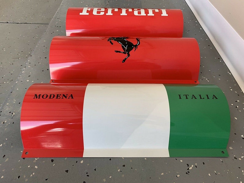 May include: Three red, white, and green cylindrical metal signs with the words "Ferrari", "Modena", and "Italia" printed on them.