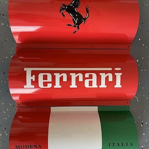 May include: A red, white, and green metal sign with the Ferrari logo, the word "Ferrari" in white letters, and the words "MODENA" and "ITALIA" in black letters.