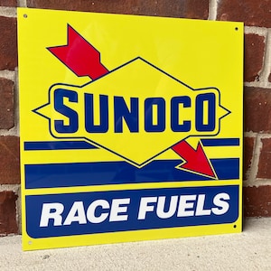 May include: Yellow metal sign with a blue and red arrow design. The sign says "Sunoco Race Fuels" in white letters.