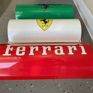 May include: Three red, white, and green cylindrical metal signs with the word "Ferrari" in white letters on the red sign. The white sign has a yellow shield with a black prancing horse logo and the letters "SF" inside the shield. The green sign has a black prancing horse logo.