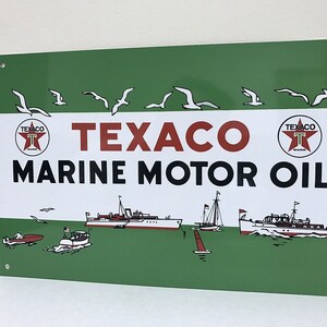 Puede incluir: Señal vintage de Texaco Marine Motor Oil con fondo verde y letras blancas. La señal presenta dos logotipos de estrellas Texaco rojas con una 'T' blanca en su interior. La señal también representa una variedad de barcos en el agua con gaviotas volando por encima.