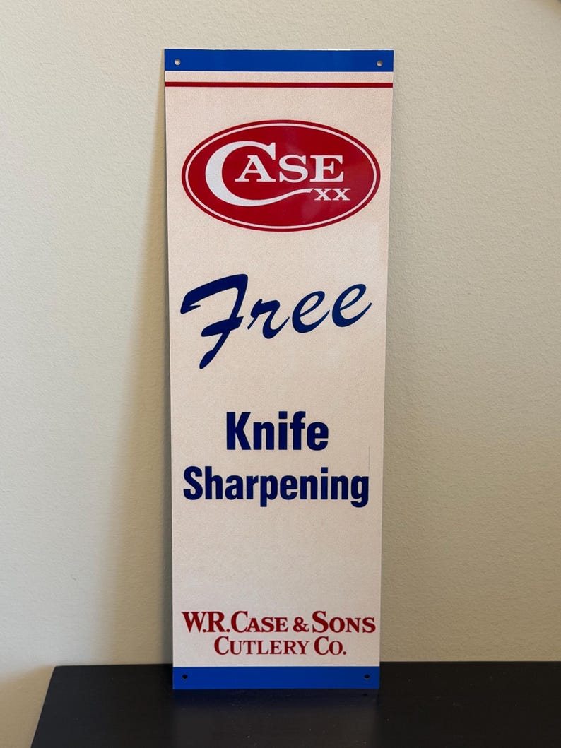 May include: A rectangular sign with a cream background, blue and red accents, and text. The top features a red oval with "CASE" in white. Below, the word "Free" is in blue script, followed by "Knife Sharpening." The bottom reads "W.R. Case & Sons Cutlery Co."