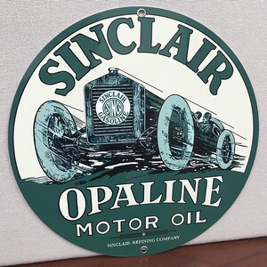 May include: A vintage Sinclair Opaline Motor Oil sign with a green background and white lettering. The sign features a black and white illustration of a vintage race car.