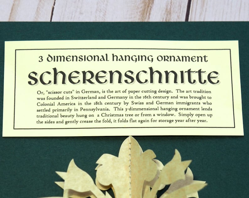 Pode incluir: Um ornamento de papel amarelo com o texto "3 dimensional hanging ornament scherenschnitte" e uma descri&ccedil;&atilde;o da forma de arte. O ornamento est&aacute; dobrado e pronto para ser montado.