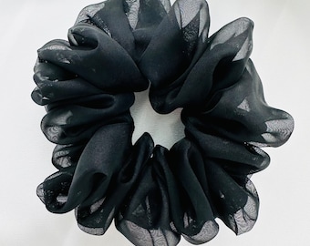 May include: A black sheer fabric scrunchie hair tie. The scrunchie is made of soft, gathered fabric and is designed to hold hair in place.