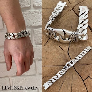Könnte beinhalten: Ein silbernes Armband mit einem klobigen Kettendesign und filigranen Details. Das Armband hat einen Verschluss und wird an einem Handgelenk getragen.