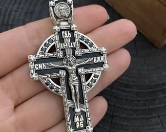 May include: A silver and black cross pendant with black gemstones. The cross features a depiction of Jesus Christ and the inscription "СВЯТЪЙ БОГЪ" in Cyrillic.