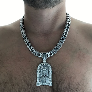 Könnte beinhalten: Eine silberne Kettenkette mit einem silbernen Anhänger mit einem religiösen Symbol. Der Anhänger hat ein verziertes Design und den Text "CT HHK".