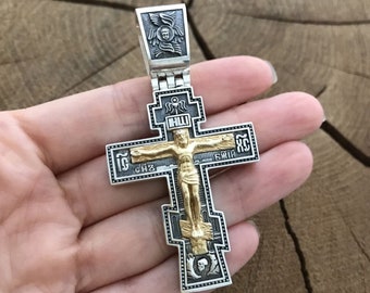 May include: A silver and gold cross pendant with intricate details and a figure of Jesus Christ on the cross. The cross is decorated with Cyrillic lettering.