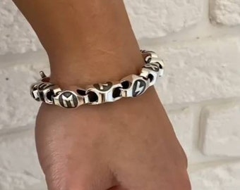May include: A silver bracelet with black and white lightning bolt charms. The bracelet is on a person's wrist.