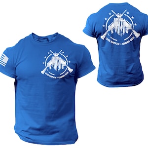 May include: A royal blue t-shirt with a white graphic of crossed rifles with an American flag in the center. The graphic is surrounded by stars and the text "One Nation - Under God".
