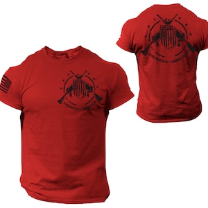 May include: Red t-shirt with a black graphic of crossed rifles, an American flag, and stars. The text "One Nation - Under God" is printed below the graphic.
