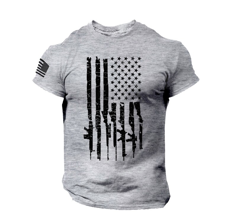 May include: A grey t-shirt with a distressed American flag design. The flag is made up of black guns instead of red and white stripes.