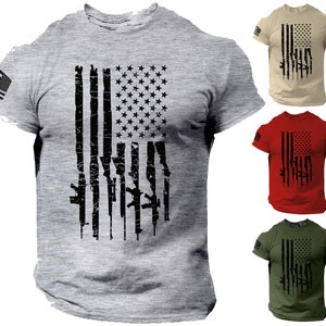 May include: A grey t-shirt with a distressed American flag design featuring a silhouette of guns. The flag is black and the guns are white. The shirt is available in other colors, including tan, red, and green.